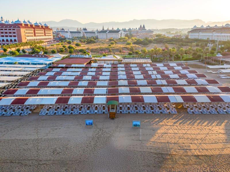 Strand mit Reihen von rot-weißen Sonnenschirmen und Liegestühlen bei Sonnenaufgang.