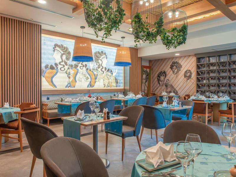 Modernes Restaurant mit Holzdecke, Pflanzen und bunten Wandgemälden in warmem Ambiente.