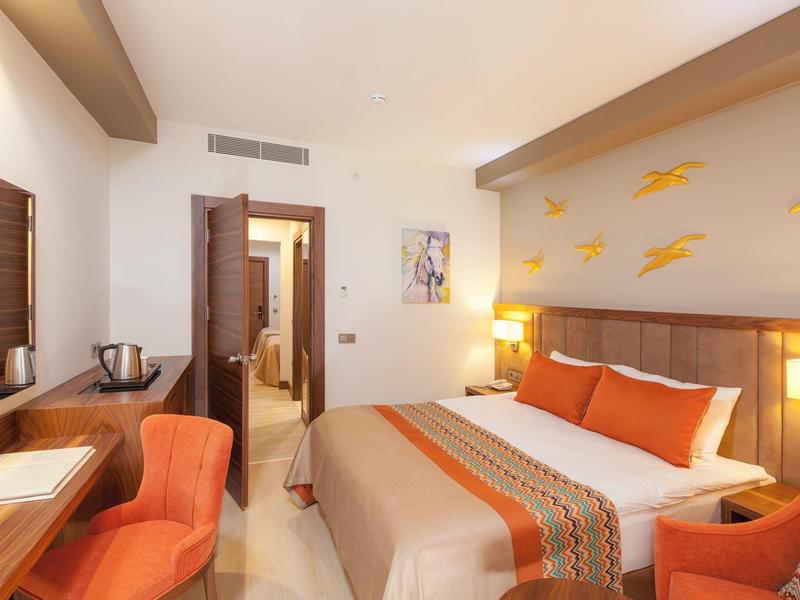 Hell eingerichtetes Hotelzimmer mit Doppelbett, orange Akzenten und modernem Mobiliar.