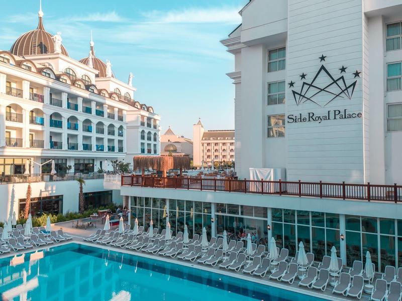 Moderner Hotelkomplex mit großem Pool und vielen Liegestühlen unter blauem Himmel.