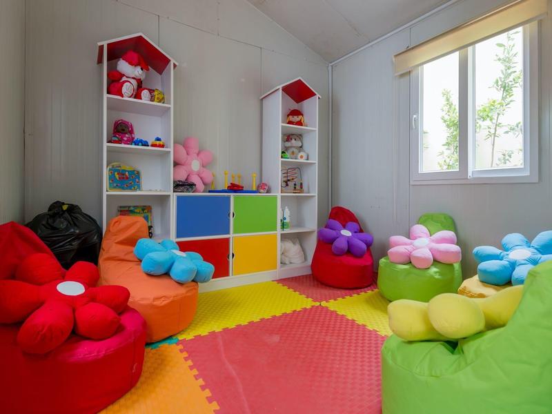 Buntes Kinderzimmer mit Sitzkissen in Blumenform, buntem Schrank und viel Spielzeug.