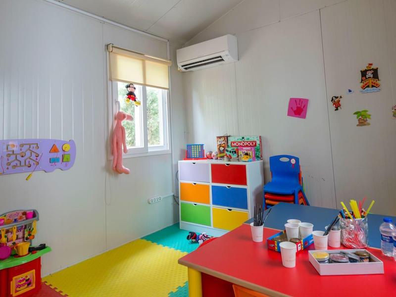 Bunter Kinderraum mit Spielzeug, bunten Regalen, Tisch mit Bastelmaterial und Luftkonditionierer.