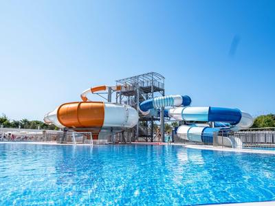 Parc aquatique avec grands toboggans colorés à côté d'une piscine bleue claire sous un ciel dégagé