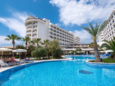 Grand bassin d'hôtel avec eau bleue entouré d'hôtels blancs et de palmiers sous un ciel bleu.