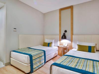 Chambre lumineuse avec deux lits simples, sol en bois moderne et accès à une pièce adjacente.