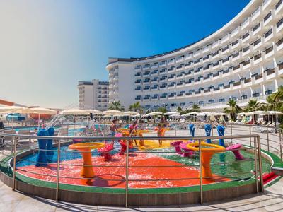 Aire de jeux aquatique colorée pour enfants devant un grand hôtel incurvé sous un ciel clair.