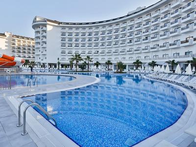Grand bâtiment d'hôtel courbé avec piscine extérieure et toboggan sous un ciel bleu clair.