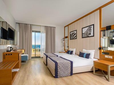 Chambre d'hôtel lumineuse avec lit double, télévision, mobilier en bois et vue sur la mer.