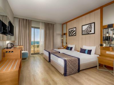 Chambre d'hôtel lumineuse avec deux lits, meubles en bois et balcon avec vue.