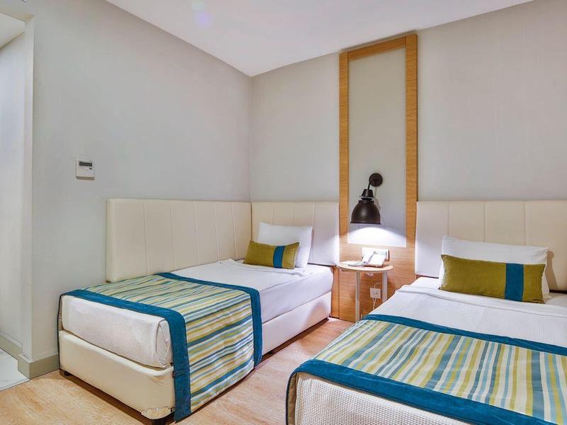 Chambre lumineuse avec deux lits simples, sol en bois moderne et accès à une pièce adjacente.