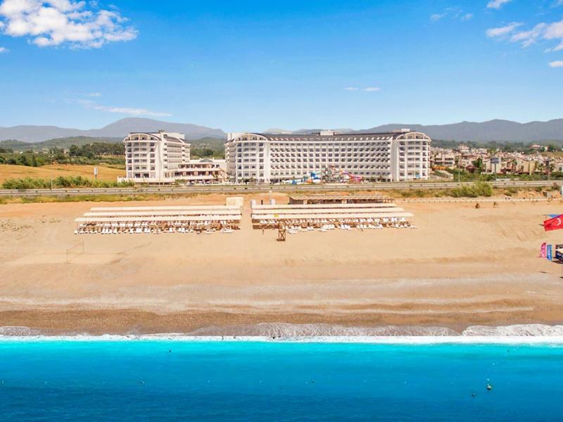 Grand hôtel sur la plage avec des transats et la mer bleue au premier plan.