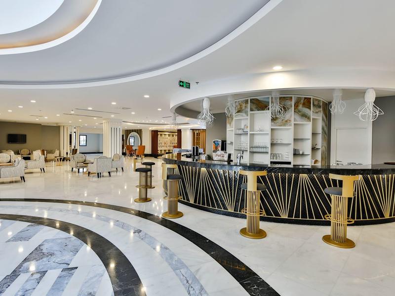 Grande hall d'hôtel moderne avec comptoir d'accueil rond, espaces assis et éclairage de plafond courbé.