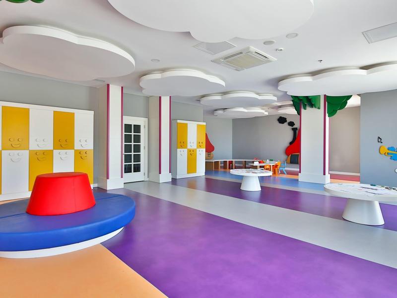 Grande salle de jeux colorée pour enfants avec sièges et peintures murales sous un éclairage lumineux.