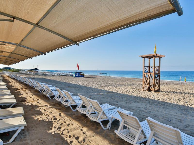 Chaises longues vides sous un abri solaire sur une plage de sable avec poste de secours et vue sur la mer.