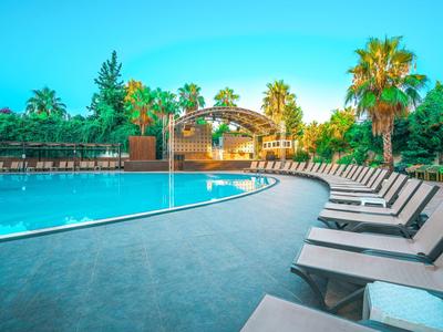 Groot zwembad met veel ligstoelen en palmbomen bij een hotelresort overdag.