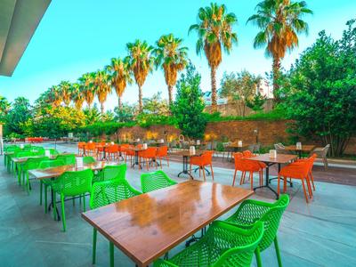 Terrazza dell'hotel con sedie verdi e arancioni e alte palme sullo sfondo.