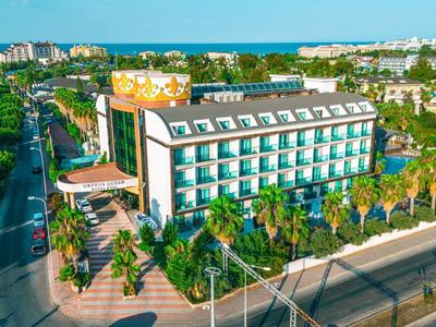 Grande edificio dell'hotel con vista sul mare, palme e strada in primo piano.