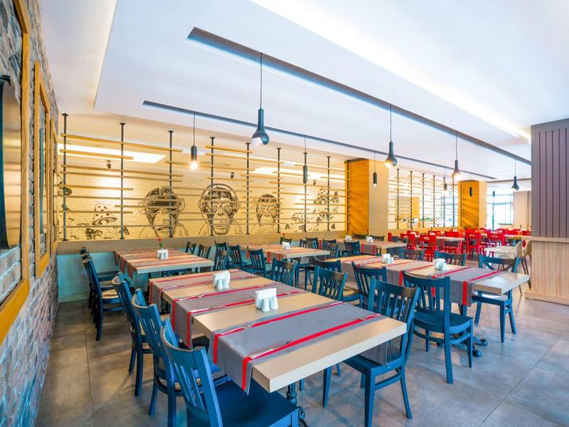 Ampia sala da pranzo con tavoli apparecchiati e sedie blu in un hotel moderno.