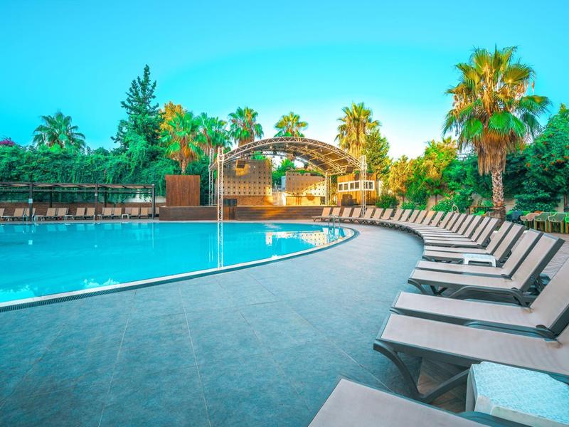 Grande piscina con molte sdraio e piante tropicali sullo sfondo.