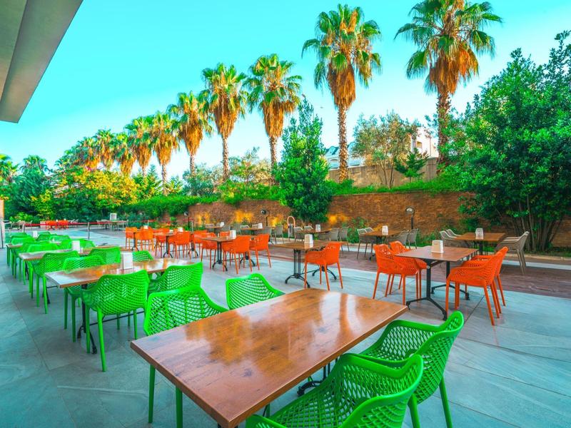 Terrazza dell'hotel con sedie verdi e arancioni e alte palme sullo sfondo.