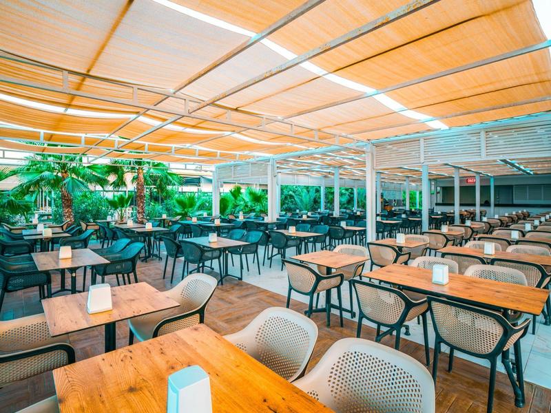 Terrazza esterna coperta con tavoli in legno e sedie grigie in un ristorante dell'hotel.