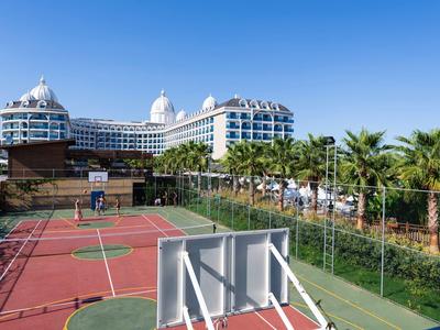 Moderner Hotelturm mit weißen Fassaden hinter einem roten Mehrzweck-Sportplatz und Palmen.