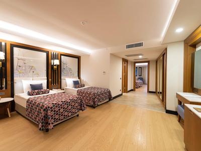 Geräumiges Hotelzimmer mit zwei Betten, Holzfußboden, modernen Lampen und langem Flur.