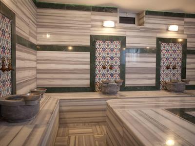 Traditionelles türkisches Bad mit Marmorwänden, Becken und Holzbänken in warmen Beige- und Brauntönen.