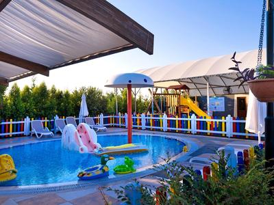 Kinderpool mit Rutsche, Sonnenschirmen und buntem Zaun, umgeben von Pflanzen und Pergolen.