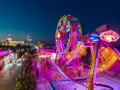 Bunte Kirmesbeleuchtung mit Riesenrad und Fahrgeschäften bei Dämmerung in einer Stadt.