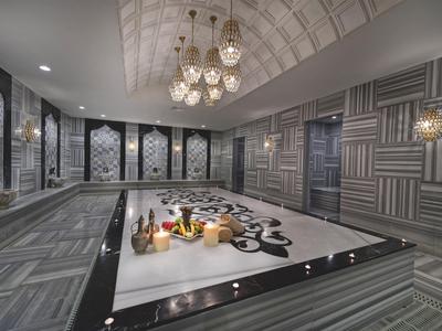 Luxuriöses türkisches Hamam mit Marmor-Mitteltisch, geometrischen Wandfliesen und Kronleuchtern.