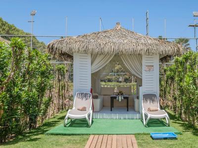 Una sala acogedora con techo de paja y dos tumbonas rodeadas de plantas verdes.