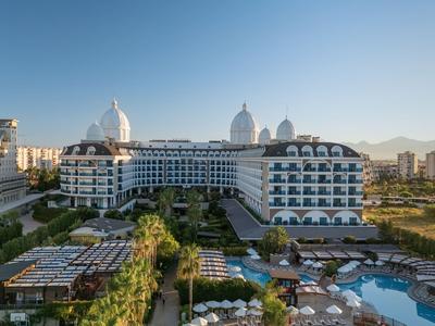 Velký vícepatrový hotel s bazénem a zahradami pod jasnou oblohou.