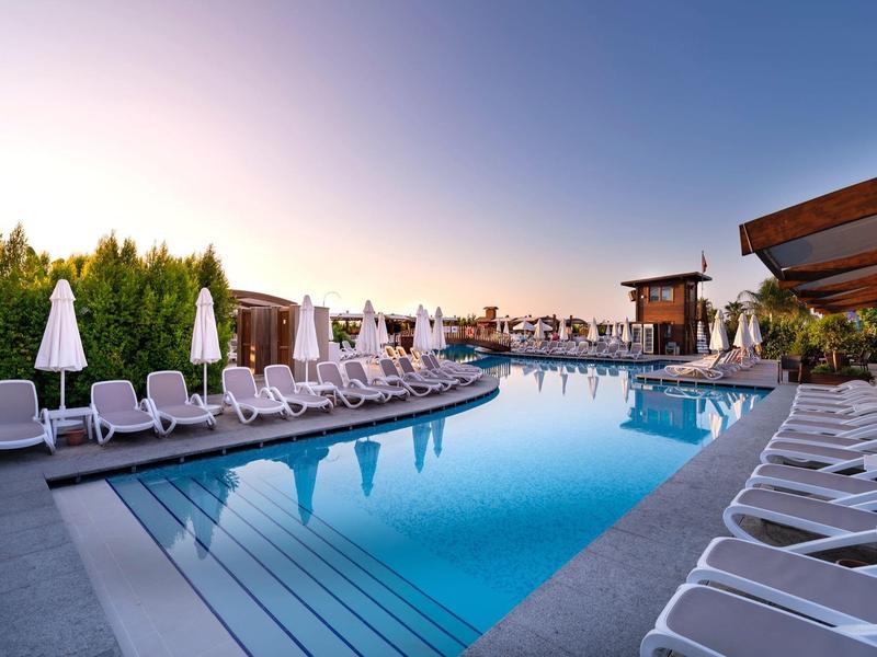 Venkovní bazén obklopený lehátky a slunečníky v moderním hotelu za soumraku.