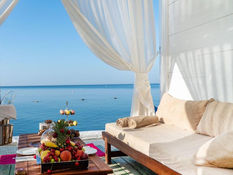 Luxusní plážový salon s bílými závěsy, pohovkou a ovocným talířem s výhledem na moře.