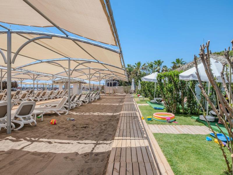 Plážové letovisko s lehátky pod slunečníky a přilehlou zahradou s barevnými polštáři.