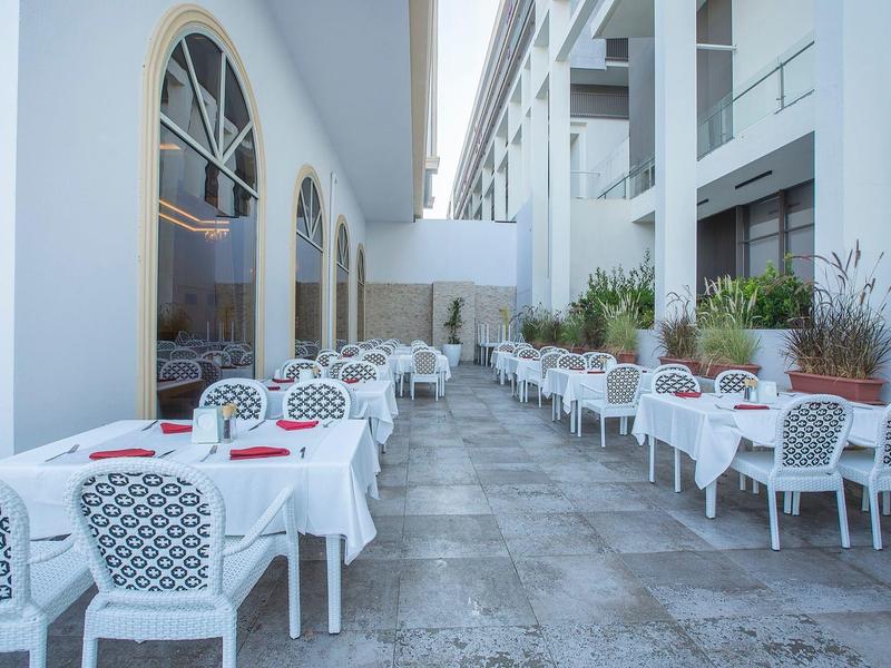 Área de comedor al aire libre con mesas y sillas blancas junto a un edificio moderno.