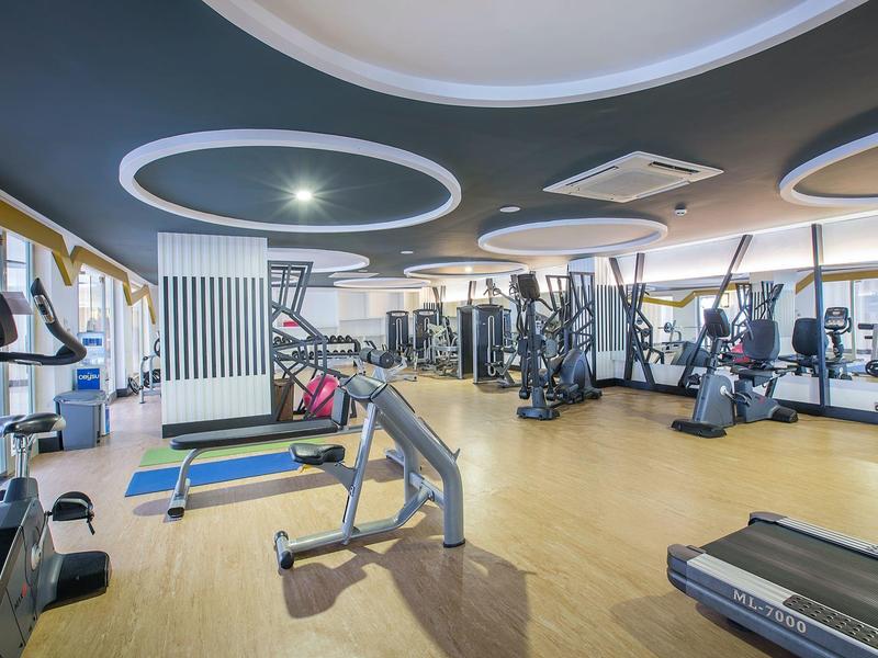 Gimnasio moderno con máquinas de cardio y pesas, suelo de madera y luces circulares en el techo.