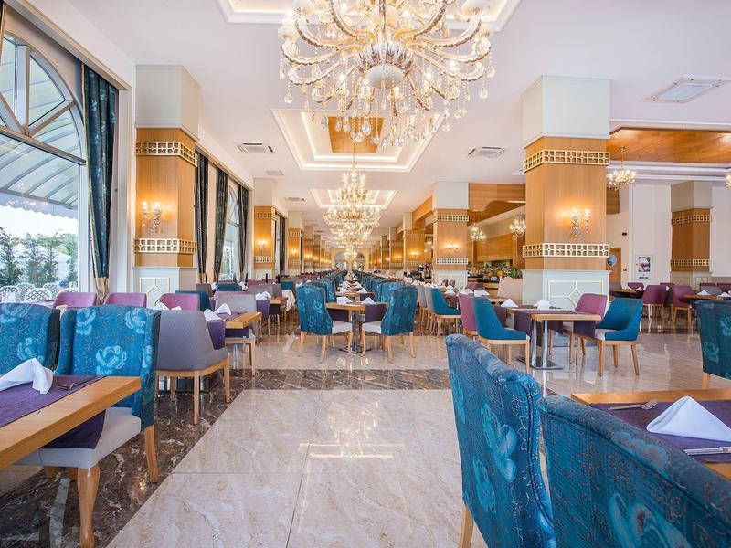 Elegante restaurante de hotel con sillas azules, grandes ventanas y candelabros en ambiente luminoso.