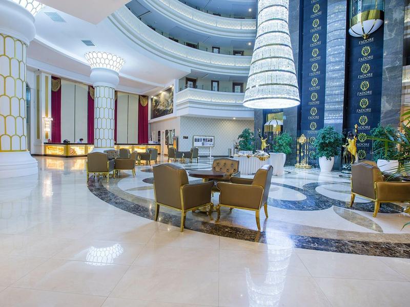 Área de lobby de hotel elegante y luminosa con grupos de asientos, suelo de mármol y techos altos.