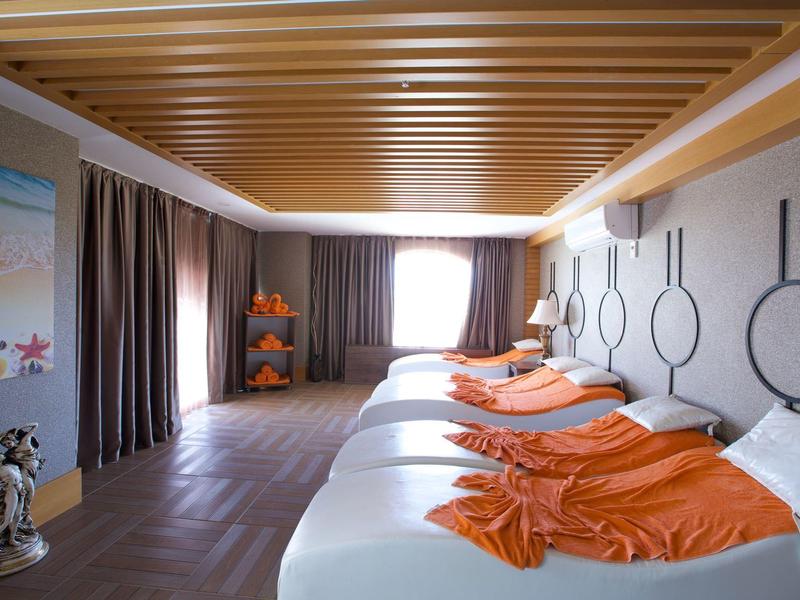 Habitación de hotel luminosa con cuatro camas decoradas con mantas naranjas y cortinas marrones.