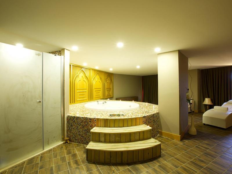 Una habitación de hotel con bañera de hidromasaje, ducha y cama en un espacio cálido con suelo de madera.