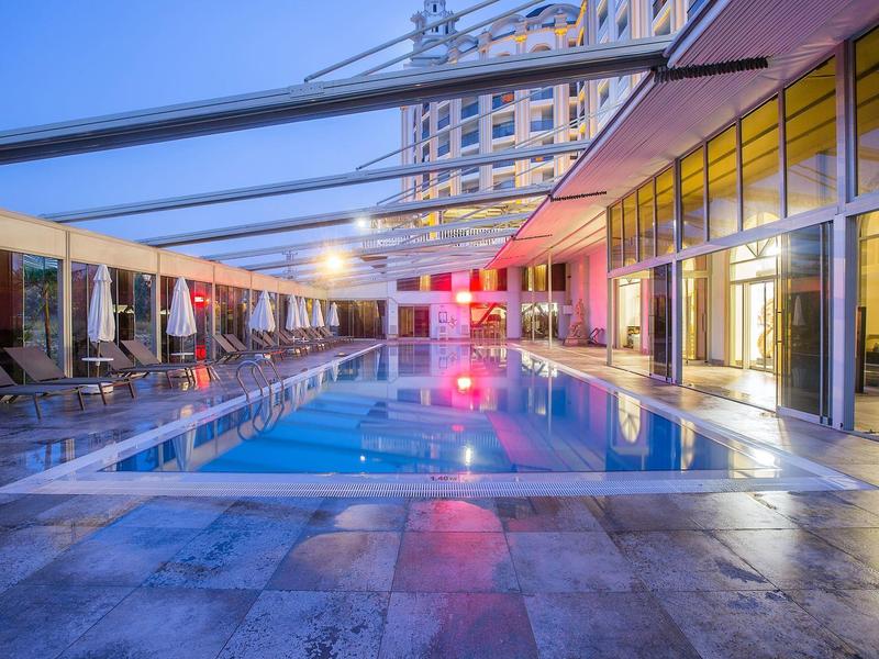 Piscina de hotel moderna con techo de vidrio y áreas de descanso al anochecer en la ciudad