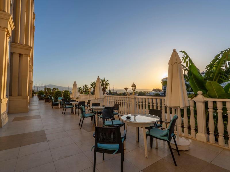 Terraza con mesas y sillas al atardecer con vista a palmeras y balcón.