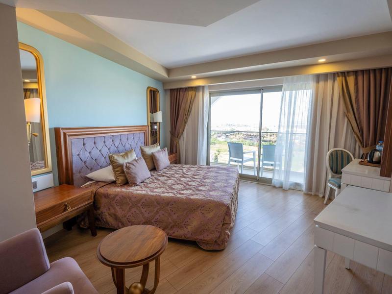 Habitación de hotel elegante con cama doble, balcón y vista al mar a la luz del día.