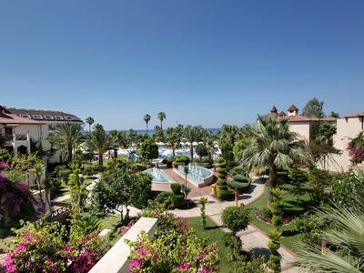 Hotel complex with pool, palm trees, and manicured garden under clear blue sky.