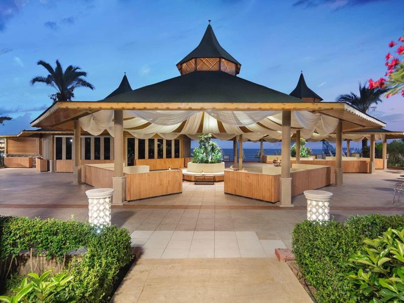 Open pavilion restaurant in a tropical hotel with palm trees and blooming plants