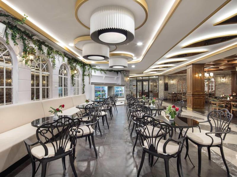 Modern hotel dining area with black chairs, white tables, and large chandeliers.