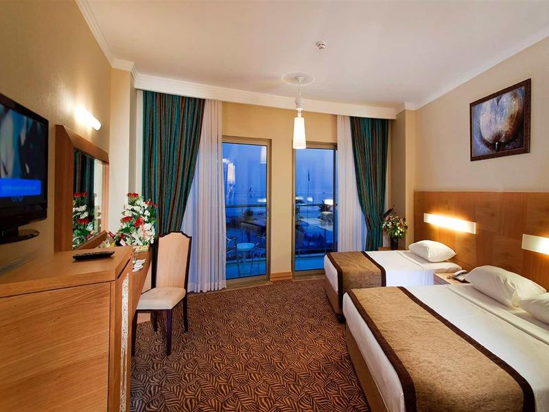 Hotel room with two single beds, desk, TV, and balcony with curtains.