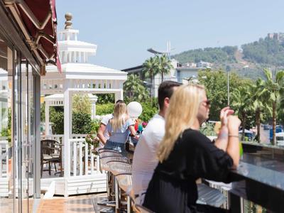 People sit and enjoy drinks on an outdoor terrace with views of palm trees and distant hills.